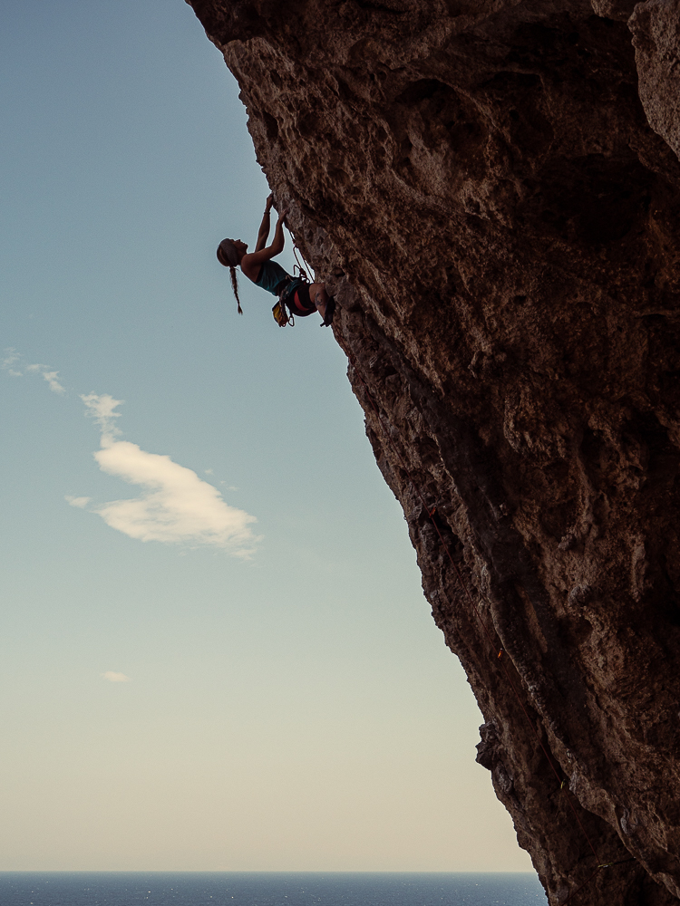 Tina climbing an overhanging rock face above the sea